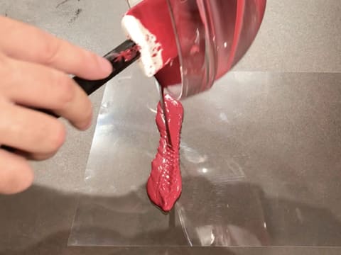 Du chocolat inspiration framboise fondu et tempéré est versé sur une feuille guitare posée sur le plan de travail