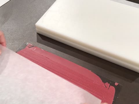 Une feuille de papier sulfurisé est posée sur la bande de chocolat inspiration framboise qui a été striée de lignes parallèles