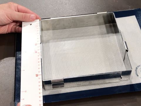 Un cadre à pâtisserie extensible mesurant 22 cm de côté, est placé sur une plaque à pâtisserie recouverte d'un tapis de cuisson en silicone