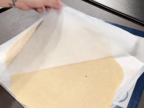 La feuille de papier sulfurisé qui recouvre le streusel amande est retirée