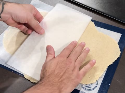 La feuille de papier sulfurisé est retirée du streusel amande qui est abaissé sur le tapis de cuisson en silicone