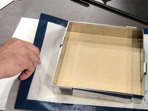 Le tapis de cuisson en silicone sur lequel il y a le streusel amande et le carré inox, est glissé sur une plaque à pâtisserie