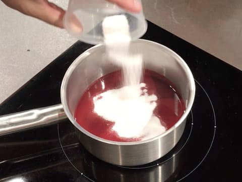 Le sucre en poudre est versé sur la purée de framboise dans la casserole qui est placée sur la plaque de cuisson