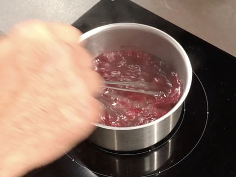 La préparation à la framboise est en ébullition dans la casserole, tout en étant mélangée au fouet