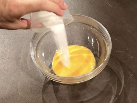 Le sucre en poudre est versé sur les jaunes d'oeufs dans le saladier en verre qui est posé sur le plan de travail