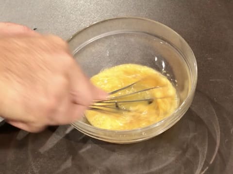 Les jaunes d'oeufs et le sucre en poudre sont mélangés au fouet dans le saladier en verre posé sur le plan de travail