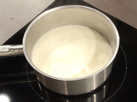 La crème fleurette est en train de chauffer dans une casserole qui est placée sur la plaque de cuisson