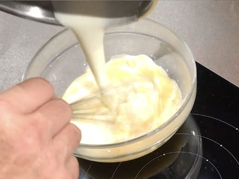 La crème liquide est versée sur le chocolat blanc fondu dans le saladier en verre, tout en étant incorporée au fouet