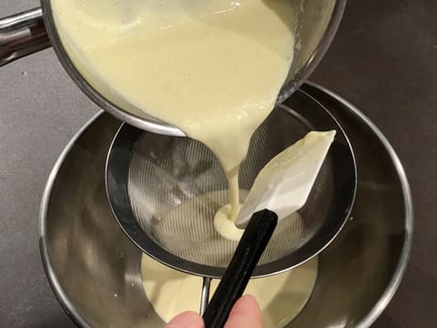 La crème au chocolat blanc est filtrée dans la passoire fine qui est posée sur le cul de poule
