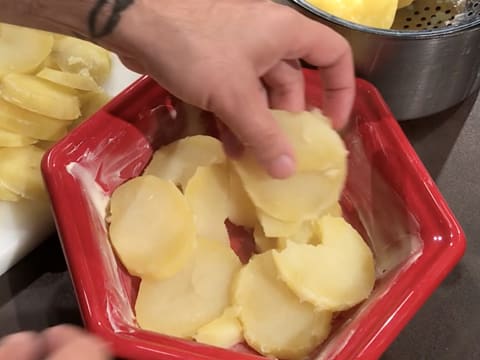 Les rondelles de pommes de terre sont disposées dans le fond du plat à gratin beurré