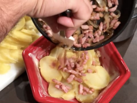 Des lardons et oignons cuits sont versés sur les rondelles de pommes de terre, dans le plat à gratin beurré