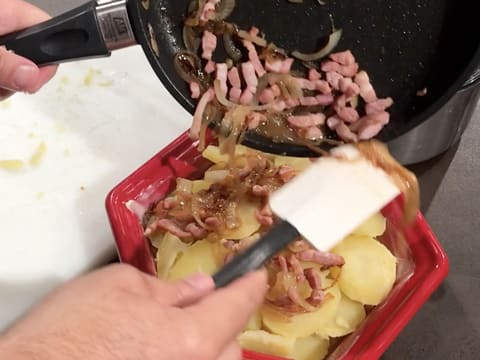 Les lardons et oignons cuits restants dans la poêle sont versés sur les rondelles de pommes de terre dans le plat à gratin