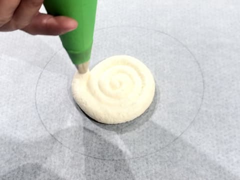 La pâte à biscuit à la cuillère est pochée en forme de spirale dans le cercle tracé au crayon à papier sur la feuille de papier sulfurisé