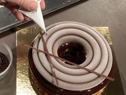 Place chocolate sticks on drops of chocolate icing over the surface of the entremets