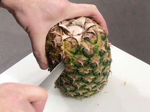 On a chopping board, cut a pineapple in half lengthwise with a knife