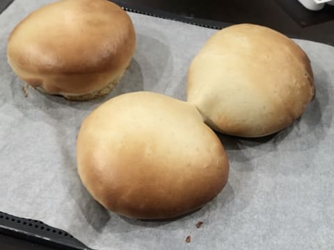 Obtention de trois beignets cuits et dorés sur la plaque de cuisson perforée recouverte d'une feuille de papier sulfurisé, qui est posée sur le plan de travail