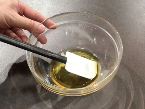 Du beurre de cacao est fondu dans un grand bol en verre qui contient également une spatule maryse