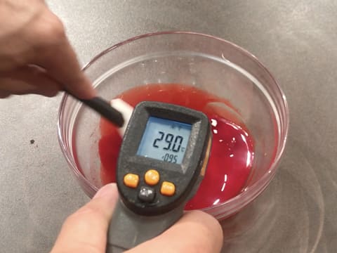 Prise de la température du beurre de cacao fondu et coloré en rouge, à l'aide d'un thermomètre à visée laser qui affiche 29,0°C