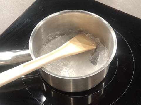 Le sirop de glucose et le sucre en poudre sont en train de cuire dans la casserole tout en étant mélangés avec une spatule
