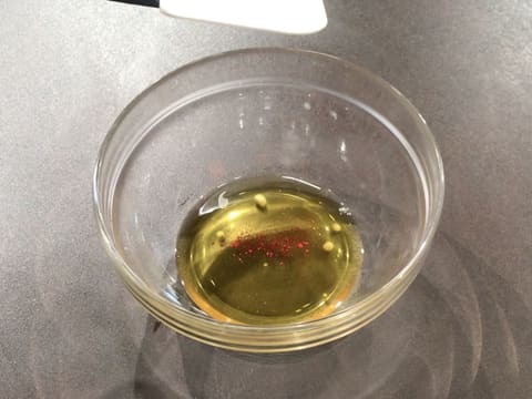 Ajout d'un peu de colorant en poudre rouge sur le beurre de cacao fondu dans le saladier en verre