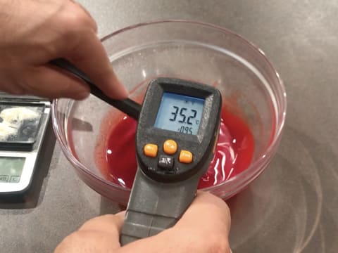 Prise de la température du beurre de cacao fondu et coloré en rouge, à l'aide d'un thermomètre à visée laser qui affiche 35,2°C