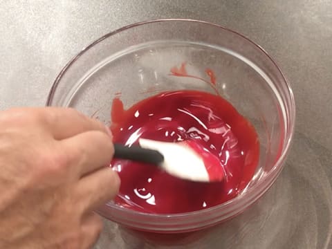 Mélange du beurre de cacao fondu et coloré en rouge dans le bol en verre avec la spatule maryse
