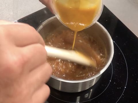 Ajout de la purée de mangue dans la sauce caramel obtenue, tout en mélangeant avec la spatule dans la casserole