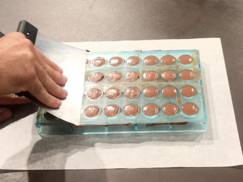 La surface du moule chocolat demi sphère dont les empreintes sont garnies de chocolat au lait tempéré, est lissée à l'aide de la spatule à chocolat