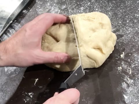 La pâte à brioche est divisée en deux pâtons à l'aide d'une spatule métallique coudée