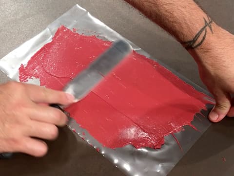 Le chocolat à la framboise tempéré est étalé sur la feuille guitare, à l'aide d'une spatule métallique coudée