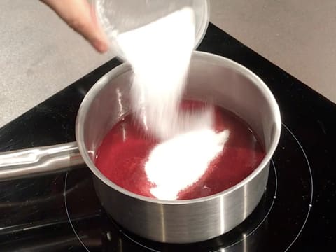 Ajout du sucre en poudre dans la casserole contenant la purée de framboise