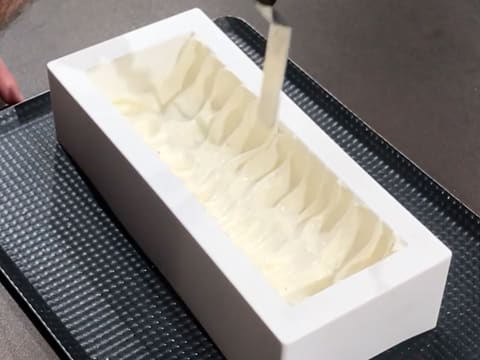 La mousse suprême vanille Tahiti est remontée sur les bords du moule à bûche en silicone, à l'aide d'une petite spatule métallique coudée