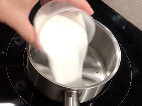 Ajout du sucre en poudre dans l'eau qui est dans une casserole