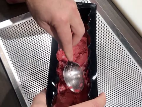 Du sorbet litchi et framboise est étalée et écrasé dans le fond du moule à bûche silicone, avec le dos d'une cuillère