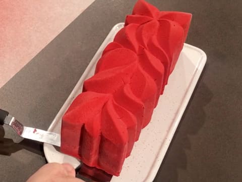 La bûche colorée est déposée sur le plat de service, à l'aide de deux spatules métalliques coudées