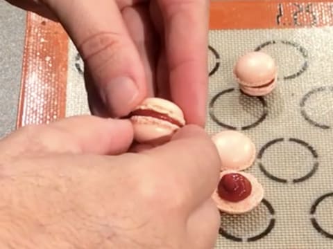 Les coques de macaron sont assemblées pour former des macarons roses garnis de confit de framboise