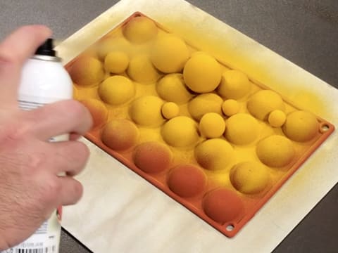Pulvérisation du colorant en spray effet velours jaune sur le deuxième côté des décors en chocolat