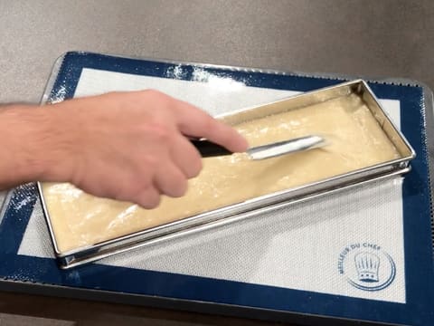 La pâte à biscuit financier est étalée avec une mini spatule coudée sur toute la surface du cadre à tarte rectangulaire