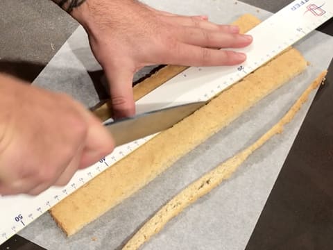 Découpe de la bande de biscuit financier sur toute la longueur à l'aide d'un couteau et d'une règle graduée