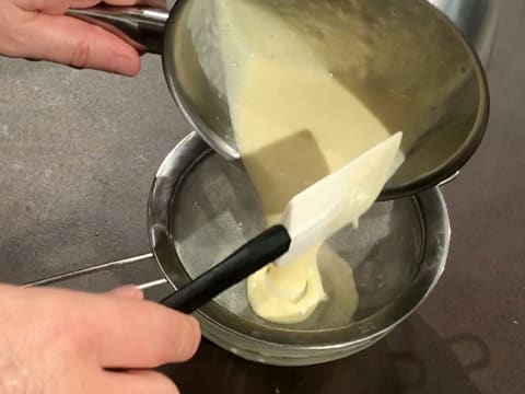 La crème anglaise est filtrée dans une passoire fine au-dessus d'un bol