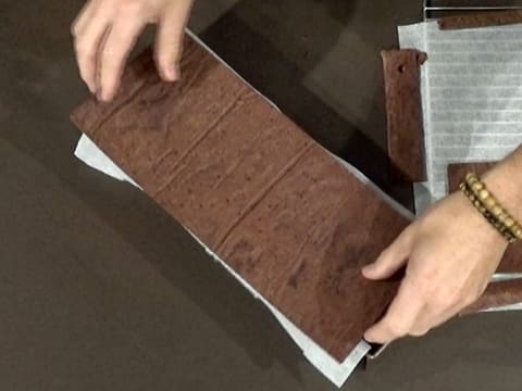 Une grande bande de biscuit chocolat est posée sur le moule à bûche chemisé de la de la feuille de papier sulfurisé