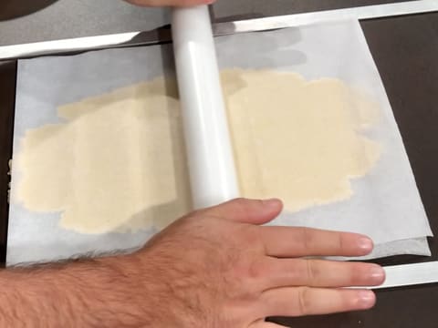 La pâte à sablé breton est abaissée entre les deux feuilles de papier sulfurisé, avec un rouleau à pâtisserie et les deux réglettes qui permettent une épaisseur régulière