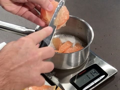 Les segments de pamplemousse sont pesés dans une casserole, elle-même posée sur une balance électronique de cuisine