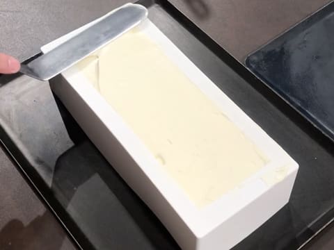 La surface de la mousse Champagne qui est dans le moule à bûche en silicone, est lissée à l'aide de la spatule métallique coudée