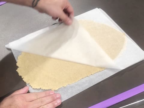 La pâte à streusel amande est abaissée de façon verticale au rouleau à pâtisserie, entre deux feuilles de papier sulfurisé et entre deux réglettes à niveler violettes