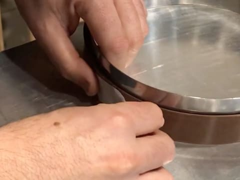 Un morceau de ruban adhésif est collé sur les deux extrémités de la bande de chocolat au lait se trouvant autour du cercle à mousse