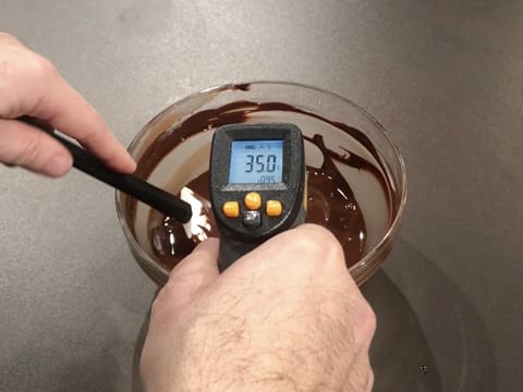 Prise de la température du chocolat noir fondu dans le saladier en verre, à l'aide d'un thermomètre à visée laser qui affiche 35,0°C