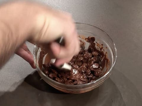 Les pistoles de chocolat noir sont à moitié fondues dans le saladier en verre, et elles sont mélangées avec la spatule maryse