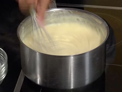 La crème pâtissière est en train de cuire dans la casserole tout en étant mélangée au fouet