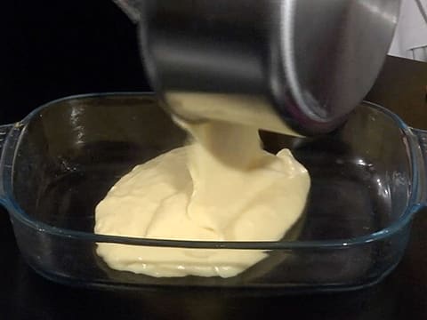 La crème pâtissière est versée dans un plat qui est posé sur le plan de travail